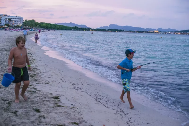 Cala Ratjada Strand an der Bucht von Alcúdia mit Bergen und Angler am Abend