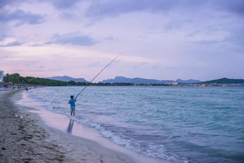 Strandmotiv von Mallorca mit Angler Angler am Strand von Mallorca bei ruhigem Meer und Bergkulisse